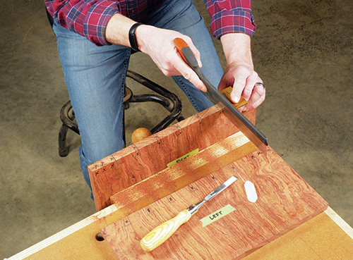 Using hand saw to cut out dovetail tails along marked lines