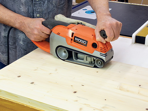 Smoothing scratches off a wood panel with belt sander