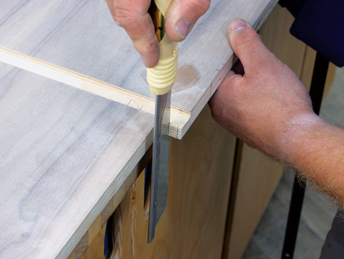 Cutting hinge pivot in cabinet panel with hand saw
