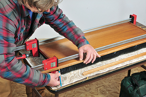 The author marks the outside length of the long trim pieces against the two pieces clamped to the short edges of the lid.